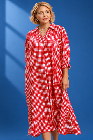 A woman modeling a red and white gingham check midi dress with three-quarter sleeves and a button-down front, set against a solid blue background with soft window shadow overlays.