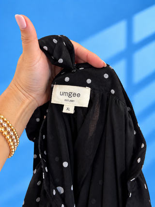 A close-up of a hand holding a black blouse with white polka dots