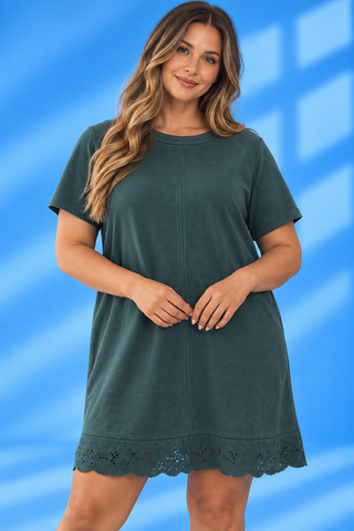 A woman modeling a short-sleeve, crew-neck tunic dress in a dark teal green color, featuring a scalloped eyelet lace hem