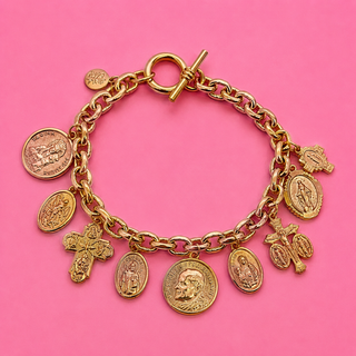 Gold charm bracelet with various charms on a pink background
