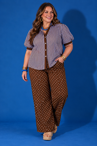 A woman modeling a short-sleeve button-up shirt with vertical blue and white stripes, brown trim