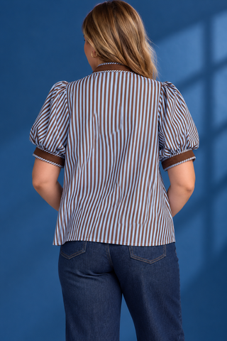 A woman modeling a short-sleeve button-up shirt with vertical blue and white stripes, brown trim