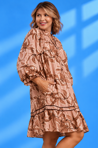 A woman modeling a metallic bronze-brown satin dress with a leaf pattern