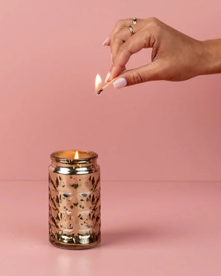 Hand lighting a candle in a decorative jar against a pink background