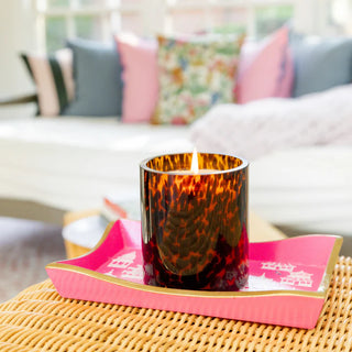 Candle in a tortoiseshell-patterned holder on a pink tray with a blurred background of a living room.