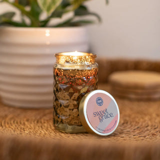 Candle in a decorative jar with 'sweet grace' label on a woven surface.