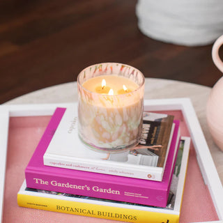 Candle burning on a stack of books with a pink and white vase in the background