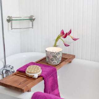 Bath tray with candle, towel, and bath brush on a bathtub
