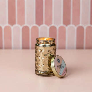 Gold candle jar with lid labeled 'Sweet Grace' on a pink background