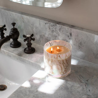 Lit candle in a decorative glass holder on a marble countertop next to a sink.