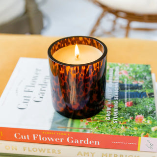 Candle in a tortoiseshell-patterned holder on a book titled 'Cut Flower Garden'.