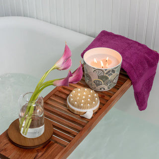 Bath tray with candle, towel, flowers, and bath brush on a bathtub.