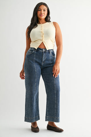 Woman wearing a cream sleeveless top and blue jeans on a white background