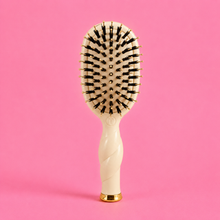 Hairbrush with a white handle and black bristles on a pink background