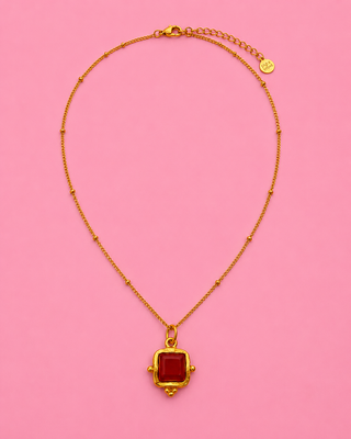 Gold necklace with a red pendant on a pink background
