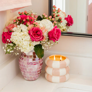 Bouquet of pink and white flowers in a mosaic-patterned vase next to a striped candle on a windowsill.