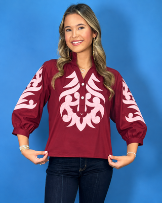Rich ruby cotton top with blush embroidered appliqué, ruffle neckline, three-quarter balloon sleeves, and button placket.