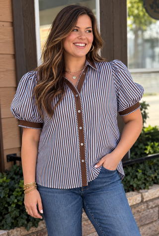 A woman modeling a short-sleeve button-up shirt with vertical blue and white stripes, brown trim