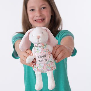 Child holding a plush toy with 'Tooth Fairy' dress against a white background