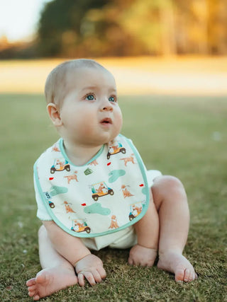 Baby sitting on grass wearing a bib with vehicle patterns