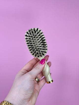 Hand holding a hairbrush against a pink background