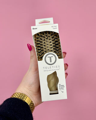 Hand holding a Teleties hairbrush packaging against a pink background