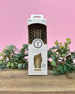 Teleties hairbrush packaging with a pink background and green plants