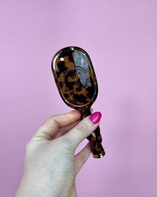 Hand holding a tortoiseshell-patterned hairbrush against a pink background