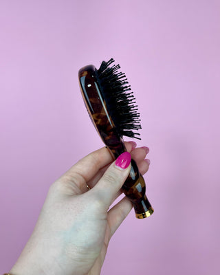 Hand holding a tortoiseshell hairbrush against a pink background