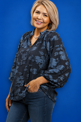 Woman wearing a dark floral blouse against a blue background