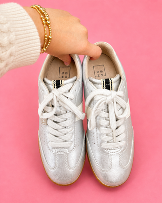 White sneakers held by a hand on a pink background