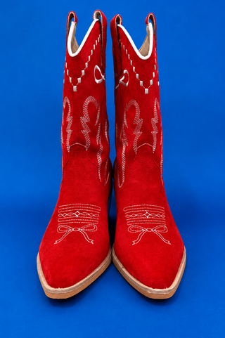 A pair of red suede cowboy boots with white western embroidery, shown against a solid blue background.