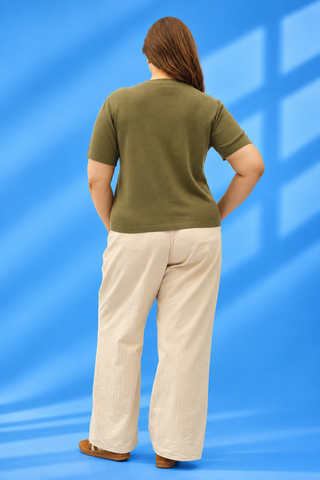 A woman shown from behind wearing an olive green short-sleeve t-shirt and light beige wide-leg trousers
