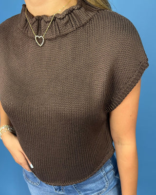 a brown short-sleeve ribbed knit top and blue jeans, standing against a solid blue background.
