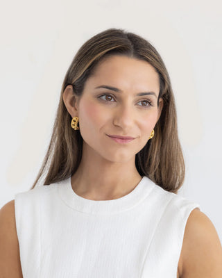 Woman wearing gold earrings against a plain background