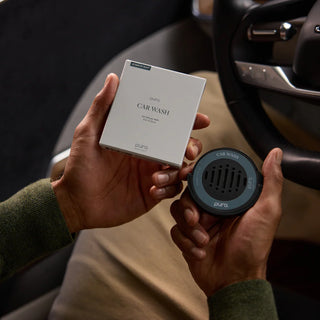 Person holding a car wash product and packaging inside a vehicle.