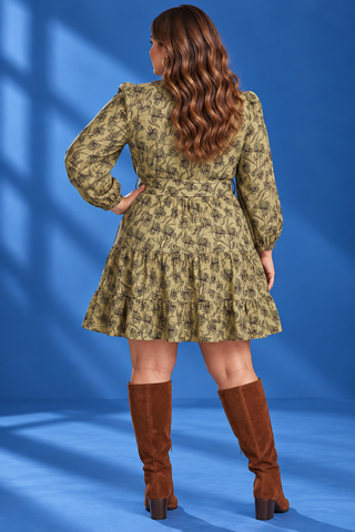 A woman modeling a long-sleeve mini dress with a brown floral pattern on a beige base, featuring a tie waist and pockets
