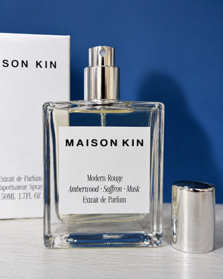 Maison Kin perfume bottle with silver cap on a blue background
