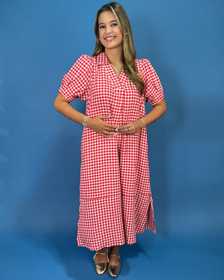 A woman modeling a red and white gingham midi dress with puff sleeves and a wrap-style neckline, standing against a solid blu