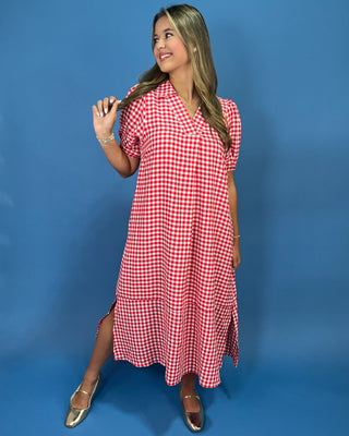 A woman modeling a red and white gingham short-sleeve midi dress with a collared neckline, standing against a solid blue