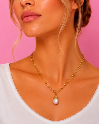 Gold chain necklace with a pearl pendant worn by a person against a pink background