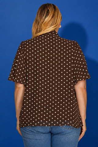 Person wearing a brown polka dot shirt against a blue background