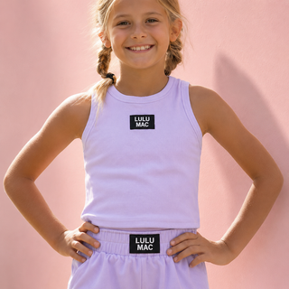 earing a light lavender sleeveless tank top and matching shorts with black rectangular patches that read 'LULU MAC' in white