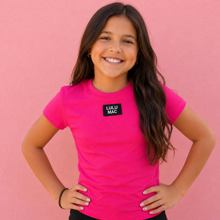 pink short-sleeve t-shirt with a black square chest patch that reads 'LULU MAC'.
