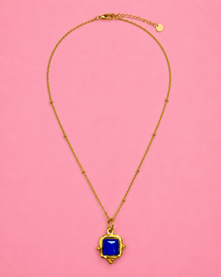 Gold necklace with a blue pendant on a pink background