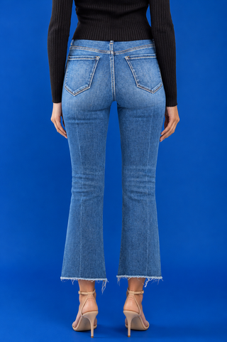 A model wearing medium-wash blue cropped flare jeans with a raw frayed hem