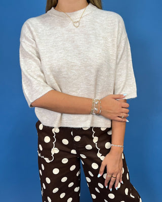 A woman modeling a cream-colored short-sleeve knit top and brown pants with white polka dots,