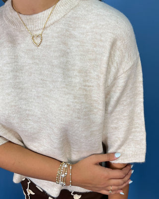 A woman modeling a cream-colored short-sleeve knit top and brown pants with white polka dots,