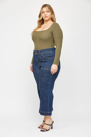 Woman wearing a green long-sleeve top and blue jeans on a white background