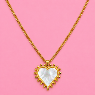 Gold necklace with a heart-shaped pendant on a pink background